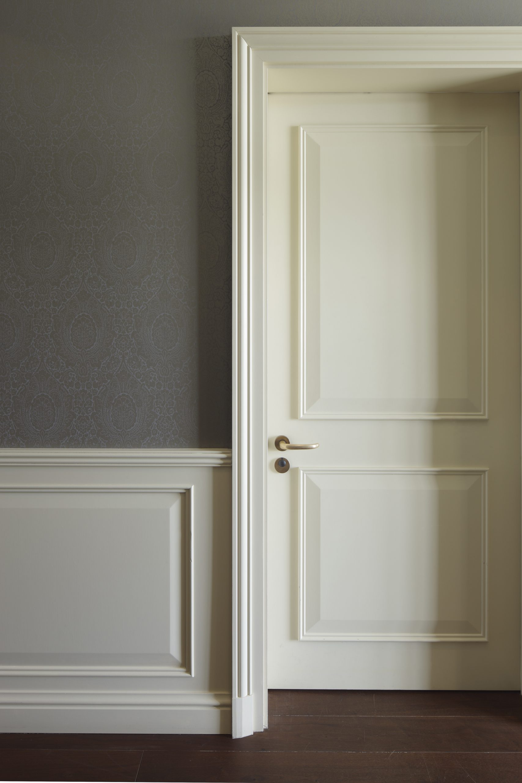 Weiße Innentür mit Messinggriff, teilweise im Schatten, eingefasst in eine graue Wand mit dekorativer Verkleidung und Tapete.
